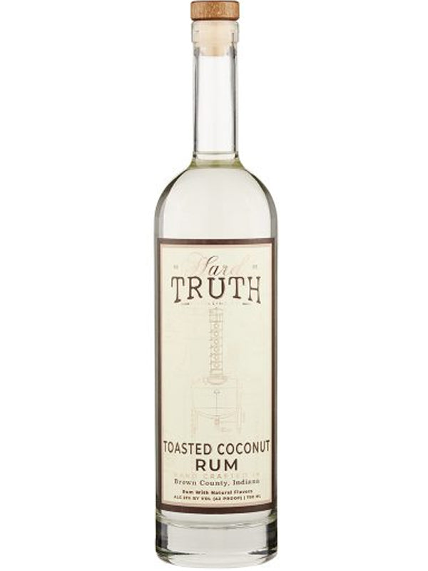 Product photography of a Hard Truth Toasted Coconut Rum bottle crafted in Brown County Indiana showcasing a clear glass bottle natural cork stopper and a cream label with a subtle distilling apparatus graphic