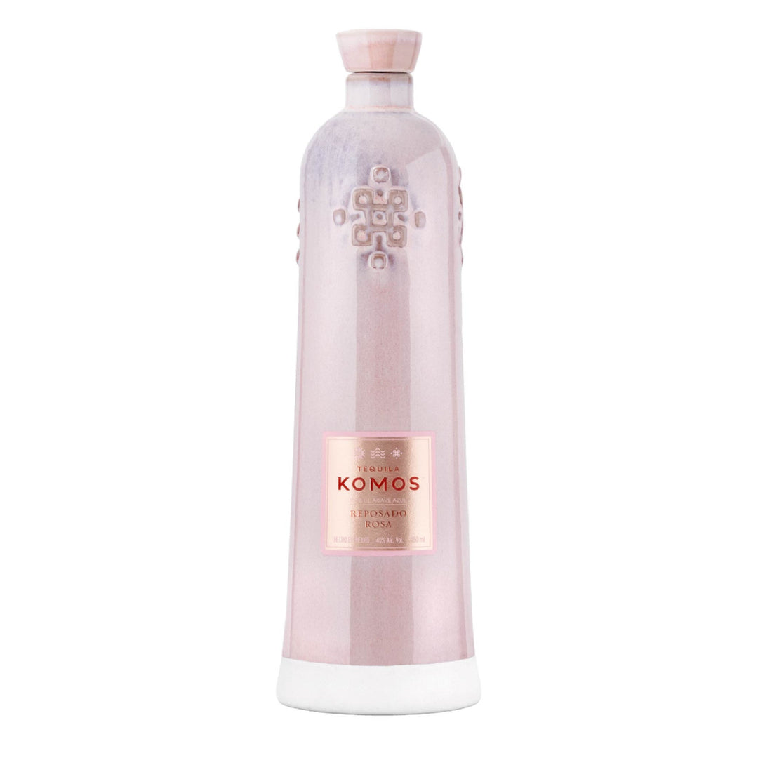 Product photography of a Komos Reposado Rosa Tequila bottle featuring a distinctive matte rose gold ceramic finish, an embossed geometric pattern, a contrasting white base, and a prominent pink label