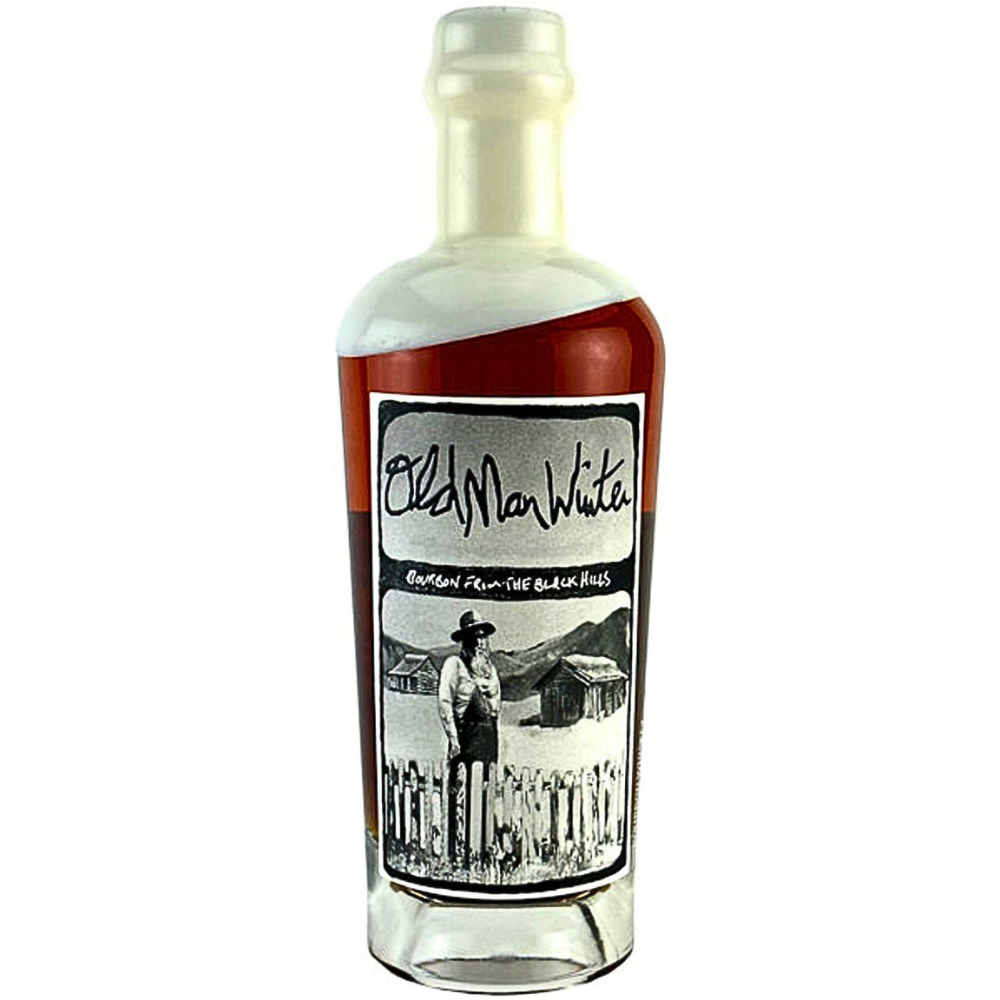 Old Man Winter Bourbon glass bottle featuring a white cap, dark amber liquid, and a black and white label depicting a bearded man in a hat and overalls amidst rustic cabins and mountains from The Black Hills