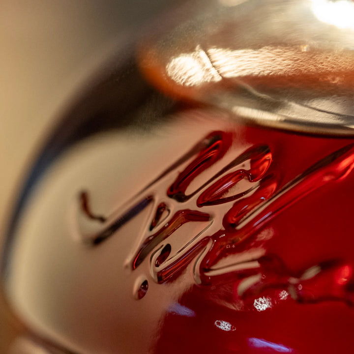 Photograph of a close-up view of a clear glass jar with embossed MASON lettering holding a deep red liquid with bright surface reflections